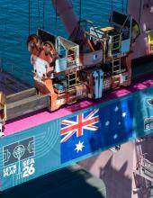A shipping container with an Australia flag banner hangs from a crane at Terminal 46 in Seattle.